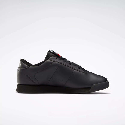 The Reebok Women's Princess Wide Shoes are classic black low-top sneakers with black laces and a subtle Union Jack logo on the heel, shown in side profile against a plain white background.