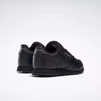 A pair of black Reebok Kids' Classic Leather Shoes - Preschool, shown from the back and side on a white background. These sneakers have a low-profile leather upper with Reebok branding on the heel and side.