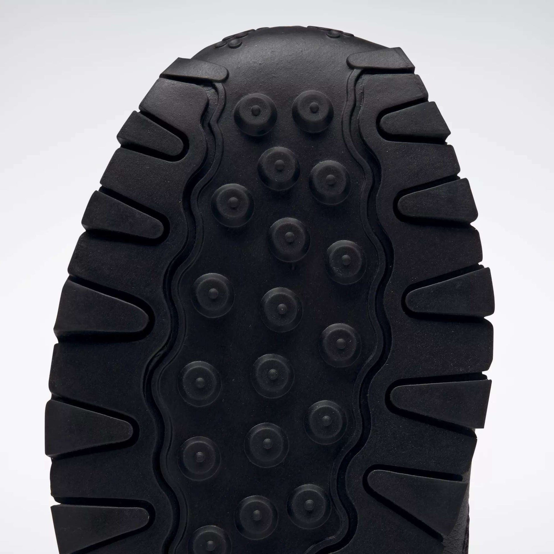 Close-up of the black sole on Reebok Kids' Classic Leather Shoes - Preschool, showing thick, rugged treads and circular indents for traction and durability, plus lightweight cushioning for all-day comfort.