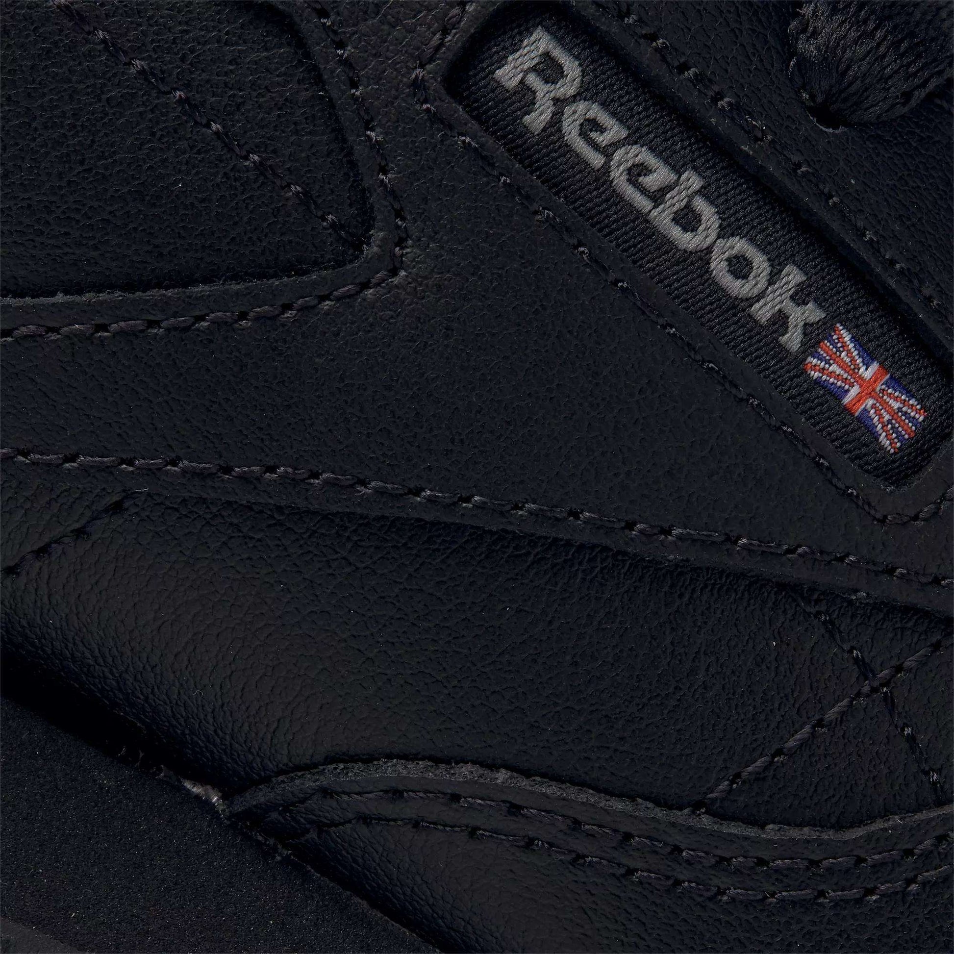 Close-up of Reebok Kids' Classic Leather Shoes - Preschool in black, showing the stitched logo and Union Jack on textured leather, designed for lightweight cushioning and all-day comfort.