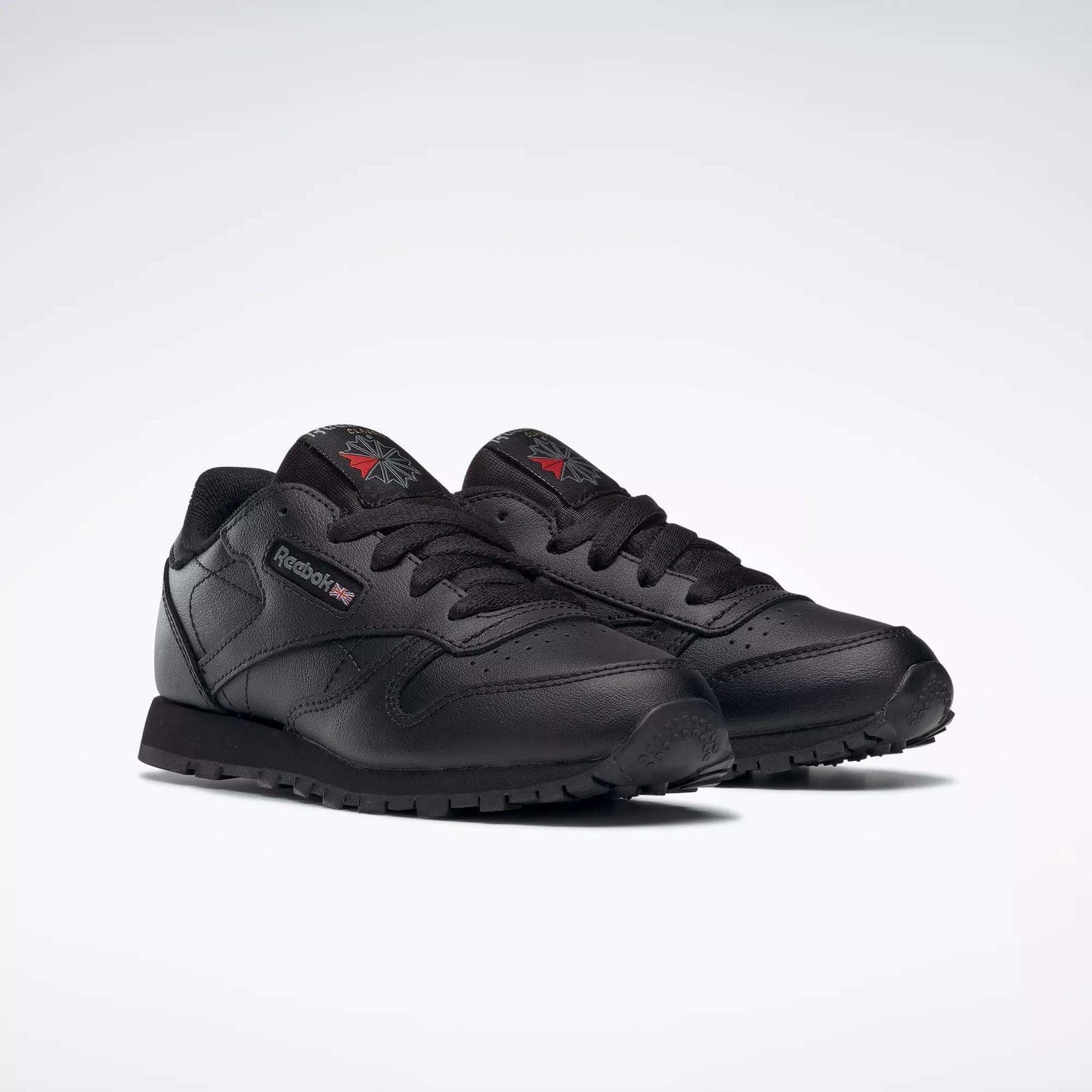 A pair of Kids' Classic Leather Shoes - Preschool by Reebok with a black leather upper, matching laces and soles, plus subtle logo accents on the side and tongue, displayed on a plain white background.