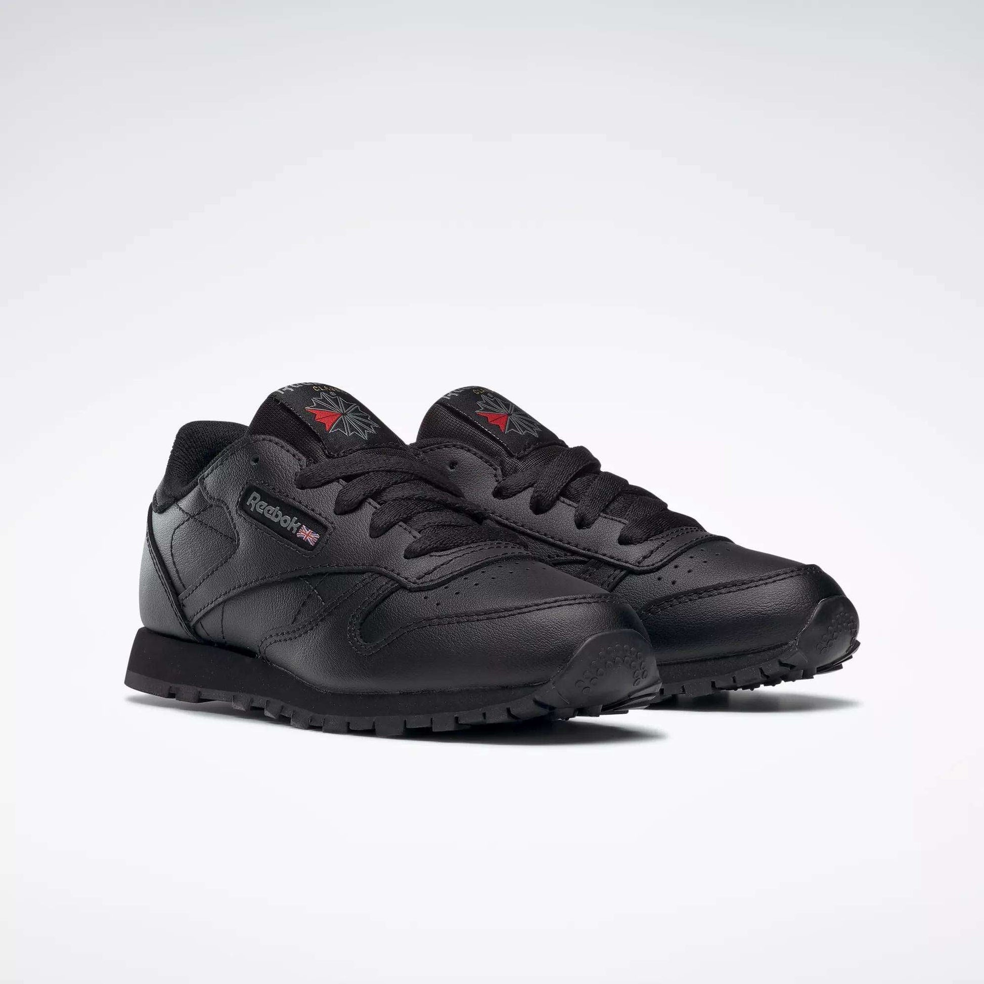 A pair of Kids' Classic Leather Shoes - Preschool by Reebok with a black leather upper, matching laces and soles, plus subtle logo accents on the side and tongue, displayed on a plain white background.