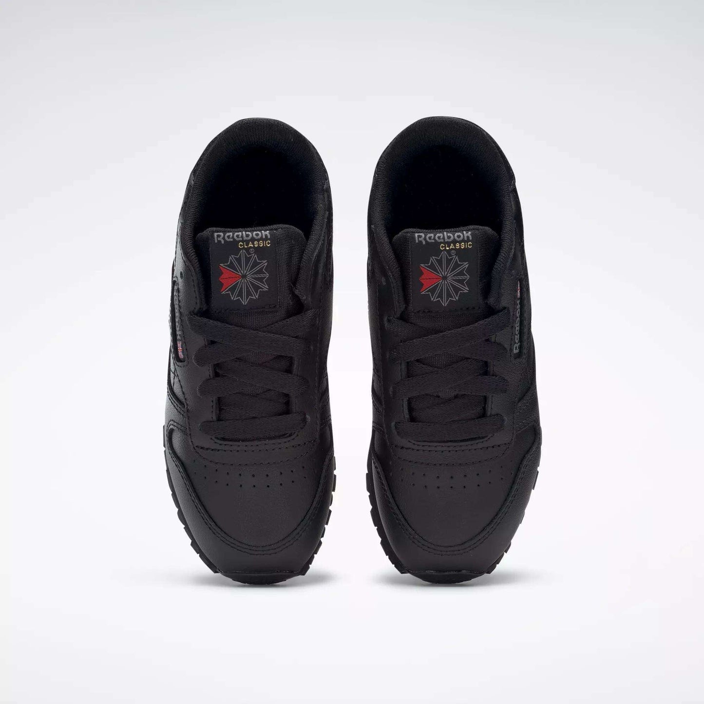 A pair of Kids' Classic Leather Shoes - Preschool by Reebok in black are shown from above, highlighting the leather uppers, laces, and Reebok logos on the tongues against a plain white background.