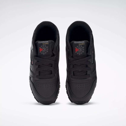 A pair of Kids' Classic Leather Shoes - Preschool by Reebok in black are shown from above, highlighting the leather uppers, laces, and Reebok logos on the tongues against a plain white background.