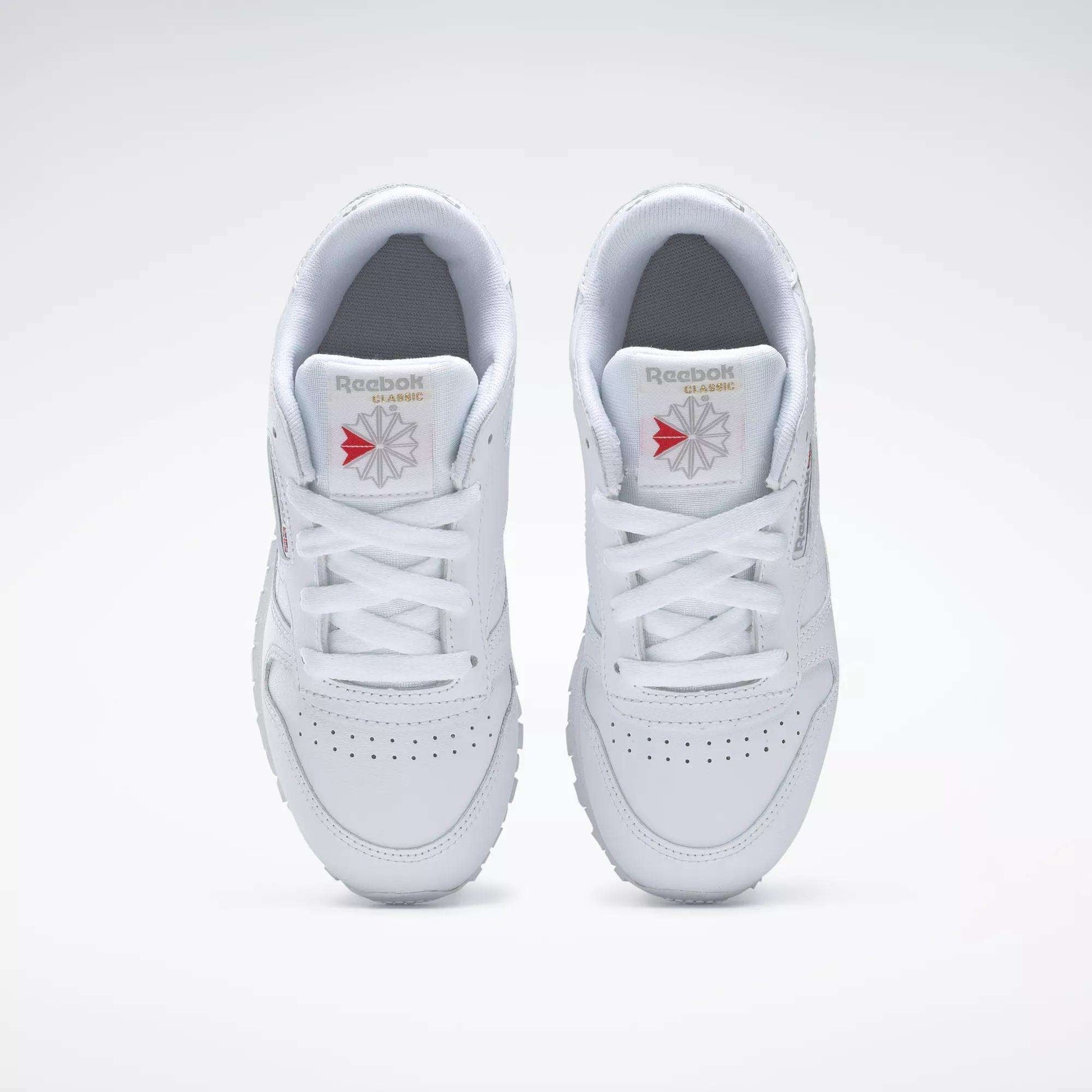 Top view of Reebok Kids' Classic Leather Shoes - Preschool, featuring a white leather upper, white laces, perforated toe boxes, and Reebok logos on the tongues against a plain white background.