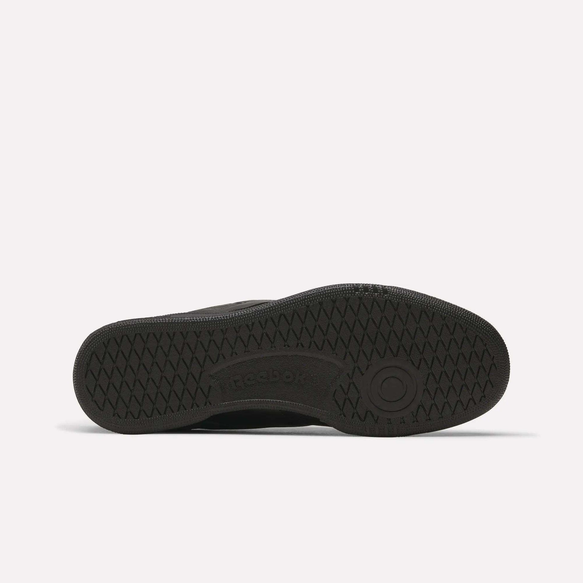 The image displays the black rubber sole of Reebok Club C 85 Shoes from beneath, highlighting a textured tread design with the Reebok logo embossed at the center.
