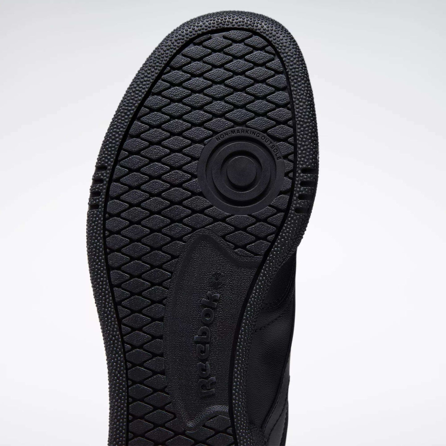 Close-up of the black rubber sole on the Reebok Club C 85 Shoes, featuring a textured hexagonal tread and circular groove, with visible Reebok branding—highlighting its tennis-inspired design.