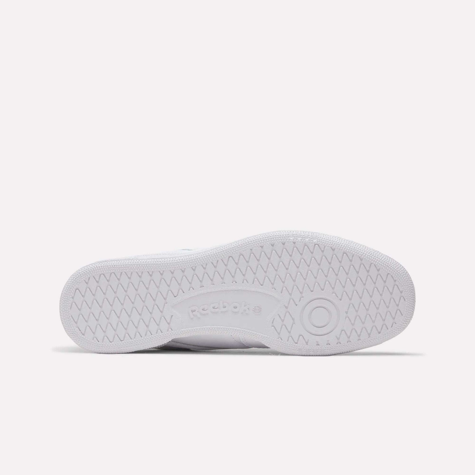The image shows the bottom view of a white Reebok Club C 85 Shoes sole, with herringbone tread patterns and the Reebok logo embossed at the center.