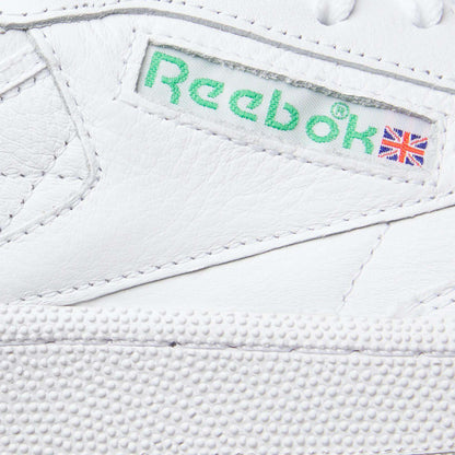 Close-up of Reebok Club C 85 Shoes in white leather, featuring a green Reebok logo and Union Jack flag on the side label, detailed stitching, and a textured rubber sole that showcases its tennis-inspired design.