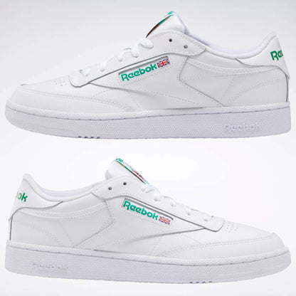 Two white Reebok Club C 85 Shoes are shown in profile, featuring green logos and Union Jack flag details on the sides, set against a plain white background to highlight their classic, tennis-inspired design.