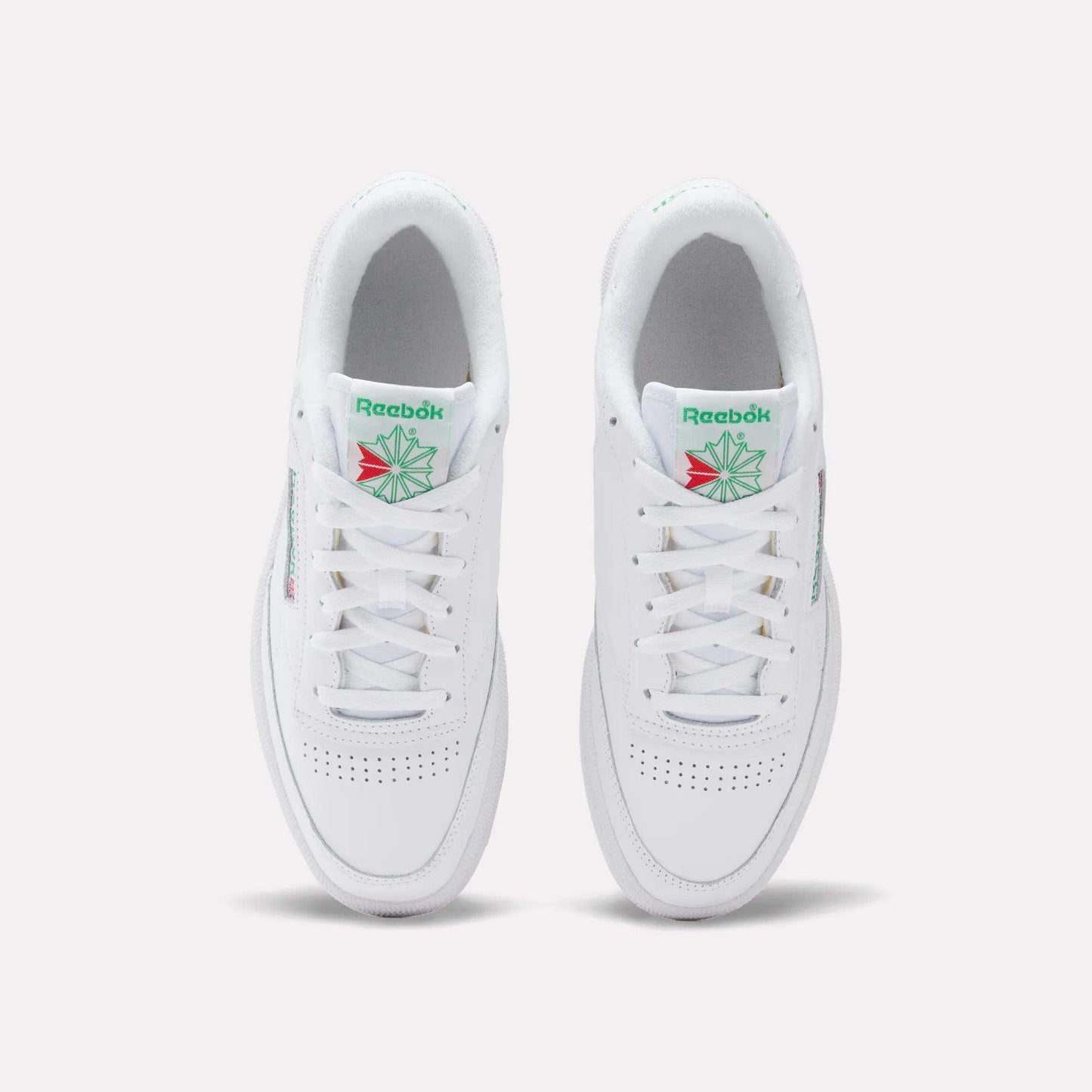 Top view of Reebok Club C 85 Shoes, featuring white leather, perforated toe, white laces, and green and red logo details on the tongue. The tennis-inspired sneakers are placed side by side on a light background.