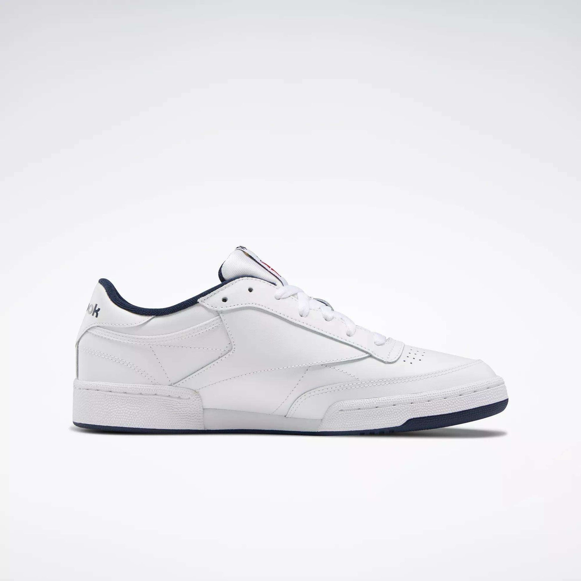 The Reebok Club C 85 Shoes are white low-top leather sneakers inspired by classic tennis style, featuring a dark blue sole and trim, simple stitching, and subtle branding on the heel and tongue.