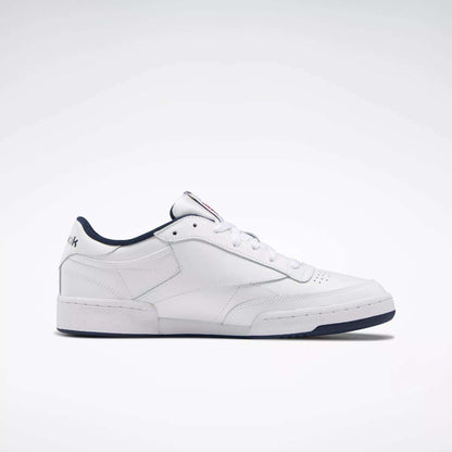 The Reebok Club C 85 Shoes are white low-top leather sneakers inspired by classic tennis style, featuring a dark blue sole and trim, simple stitching, and subtle branding on the heel and tongue.