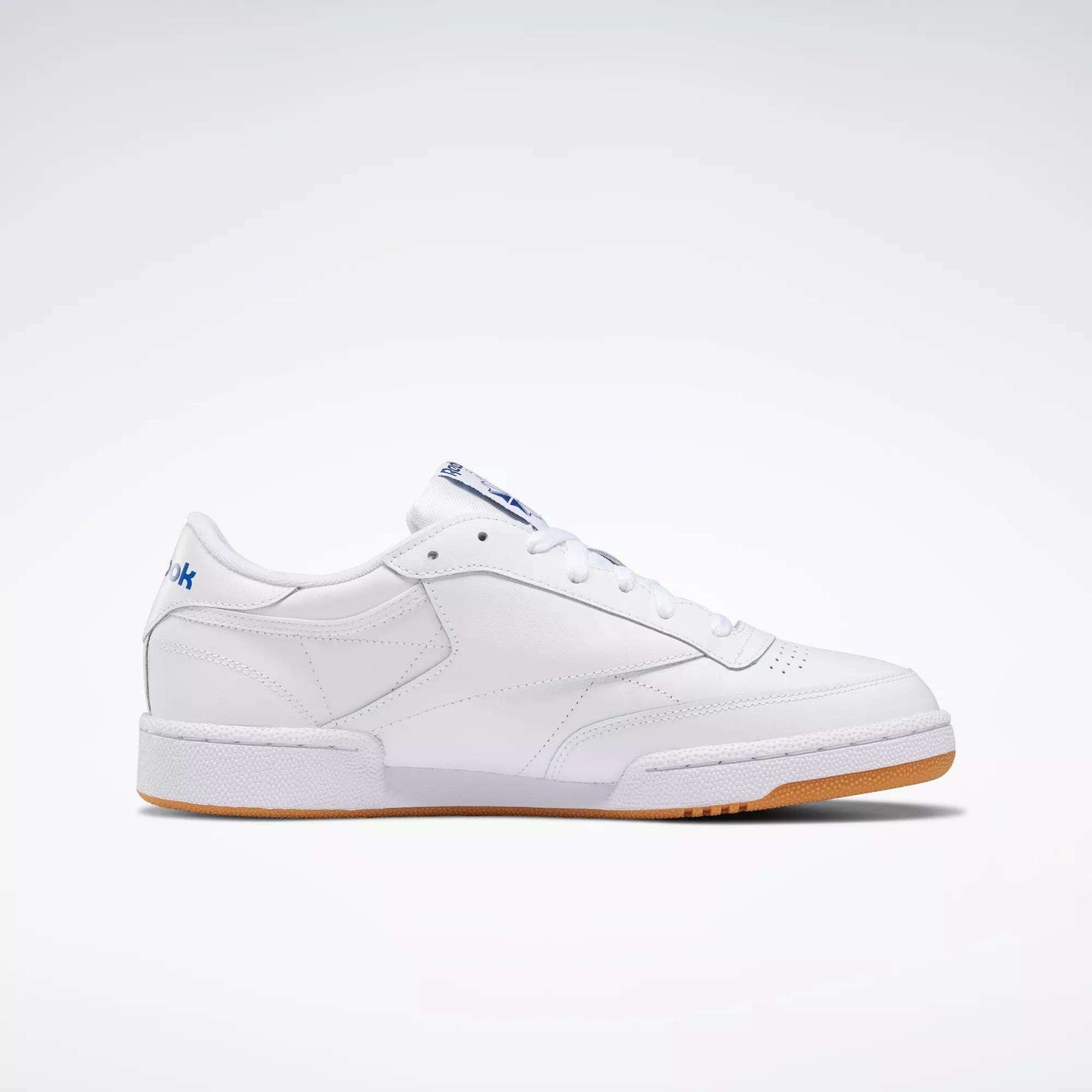 The Reebok Club C 85 Shoes are low-top white leather sneakers with a simple design, white laces, gum sole, and subtle blue branding on the heel and tongue, shown against a plain white background.