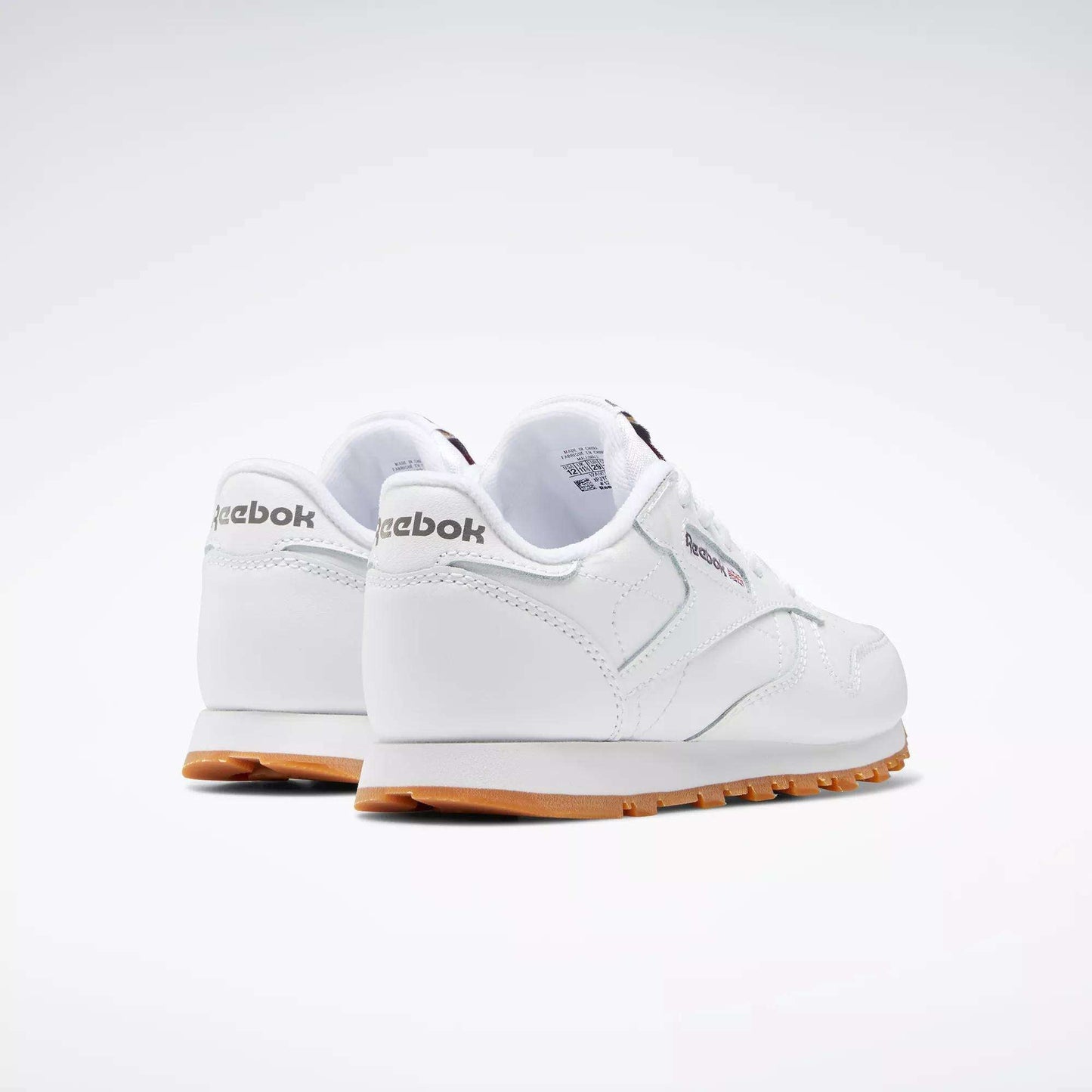A pair of Kids' Classic Leather Shoes - Preschool by Reebok in white, featuring leather uppers and gum soles, is shown from the back and side on a plain light background.