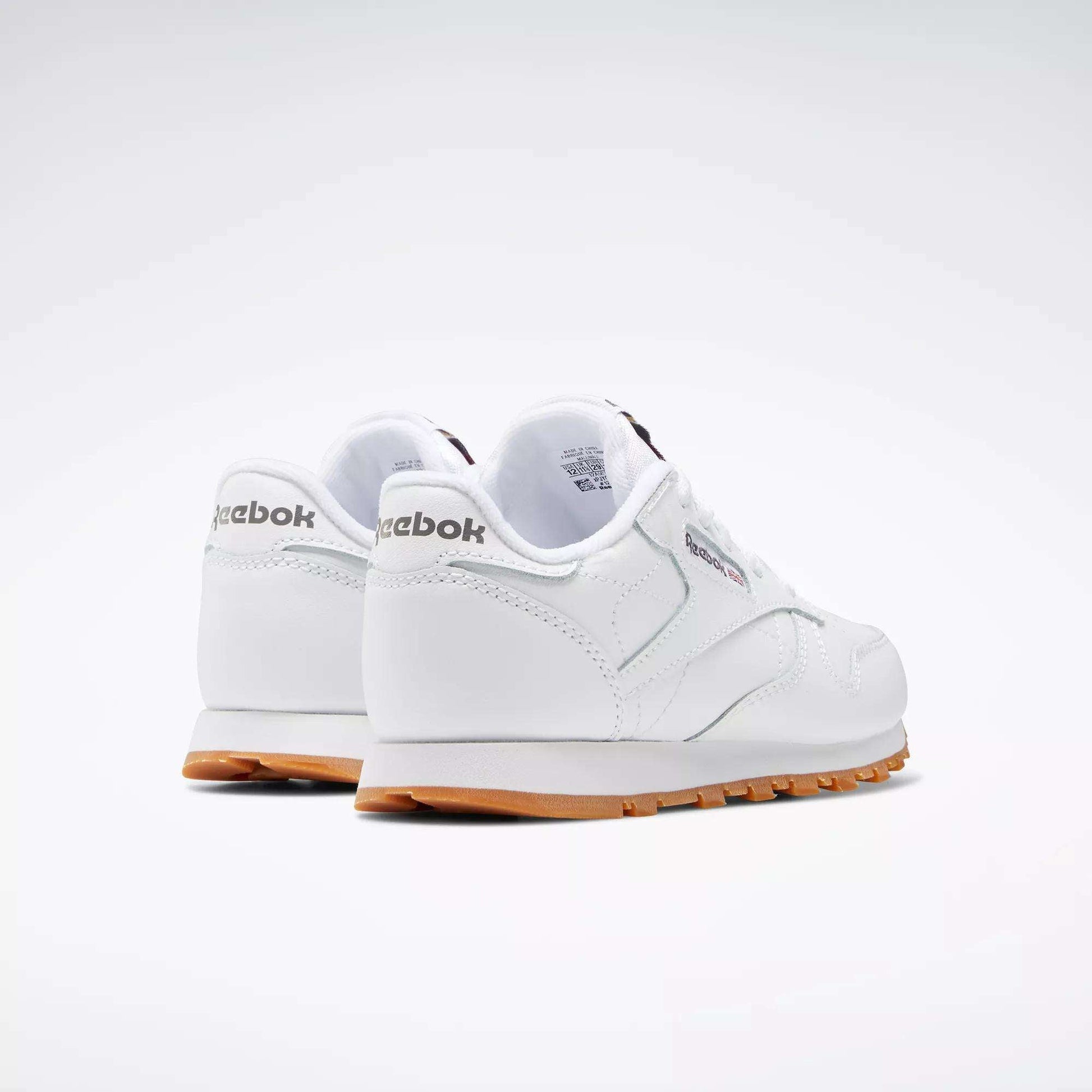 A pair of Kids' Classic Leather Shoes - Preschool by Reebok in white, featuring leather uppers and gum soles, is shown from the back and side on a plain light background.