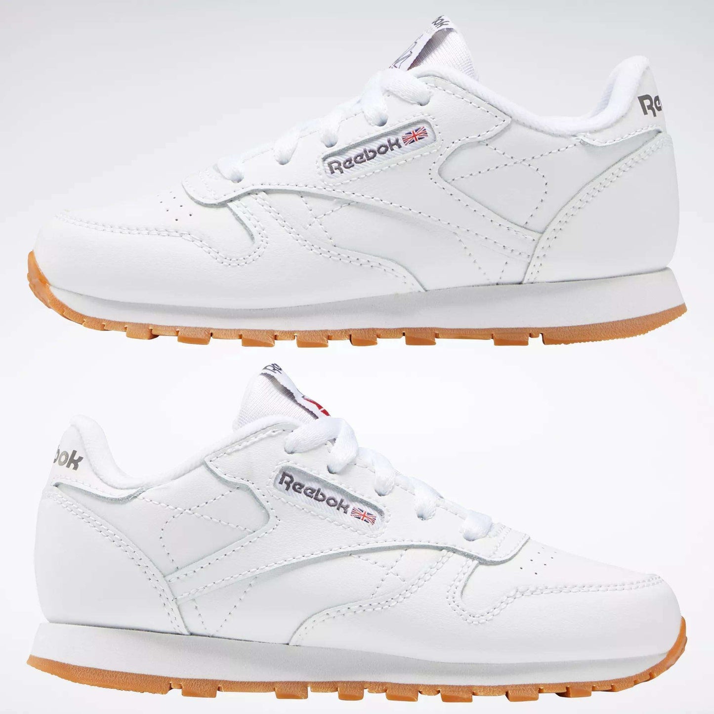 Two Kids' Classic Leather Shoes by Reebok in white are displayed side by side, showing the outer and inner sides. They feature a leather upper, Reebok branding, subtle stitching, and lightweight cushioning for comfort.