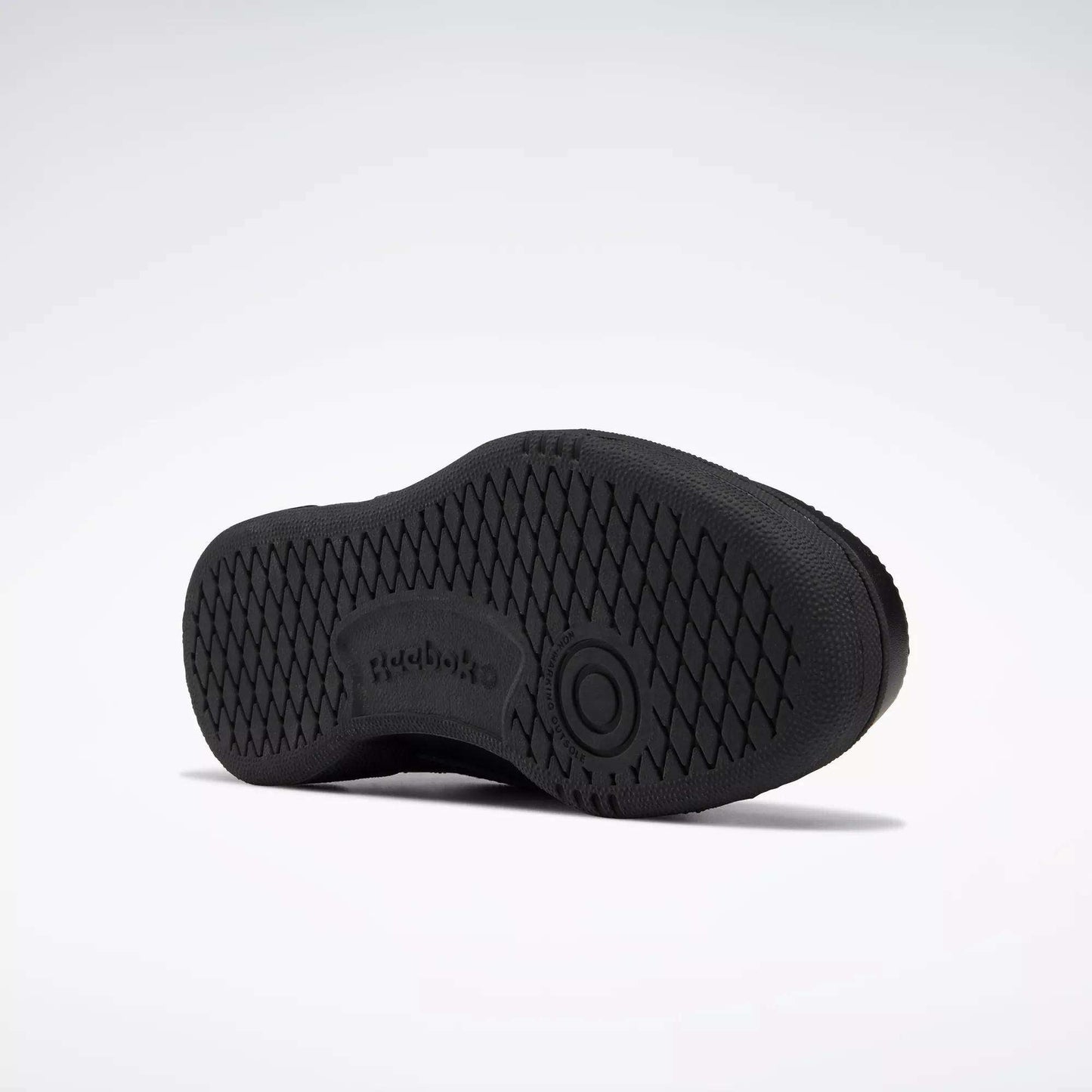 The image shows the sole of a black Reebok Kids' Club C Shoe - Grade School, with a high-abrasion rubber outsole, diamond-patterned grip, Reebok logo, and a circular design at the center. The background is plain white.