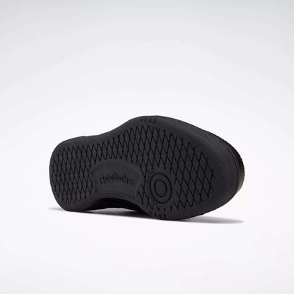 The image shows the sole of a black Reebok Kids' Club C Shoe - Grade School, with a high-abrasion rubber outsole, diamond-patterned grip, Reebok logo, and a circular design at the center. The background is plain white.