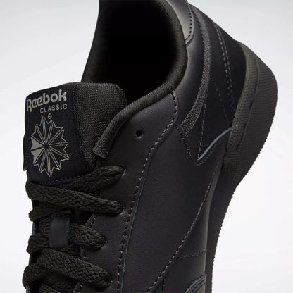 Close-up of black Reebok Kids' Club C Shoes (Grade School), featuring smooth leather uppers, the tongue with Reebok logo and starburst design, black laces, and detailed stitching.