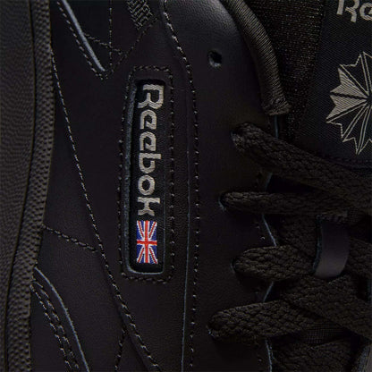 Close-up of black Reebok Kids' Club C Shoes - Grade School, showcasing classic court style with detailed stitching on soft leather uppers, plus the Reebok logo and a small UK flag patch near the laces.