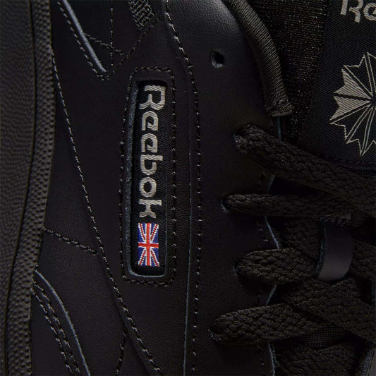 Close-up of black Reebok Kids' Club C Shoes - Grade School, showcasing classic court style with detailed stitching on soft leather uppers, plus the Reebok logo and a small UK flag patch near the laces.