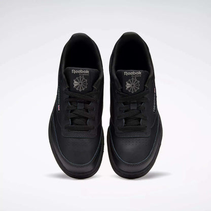 A pair of Kids' Club C Shoes - Grade School by Reebok, in black leather with perforated toe details, are shown from above. The classic court design features black laces and logos, positioned side by side on a plain light background.
