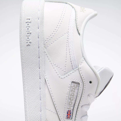 A close-up side view of the Reebok Kids' Club C Shoes - Grade School displays soft white leather uppers, clean minimal stitching, a textured sole, "Reebok" embossed on the side, and the Union Jack flag near the sole.