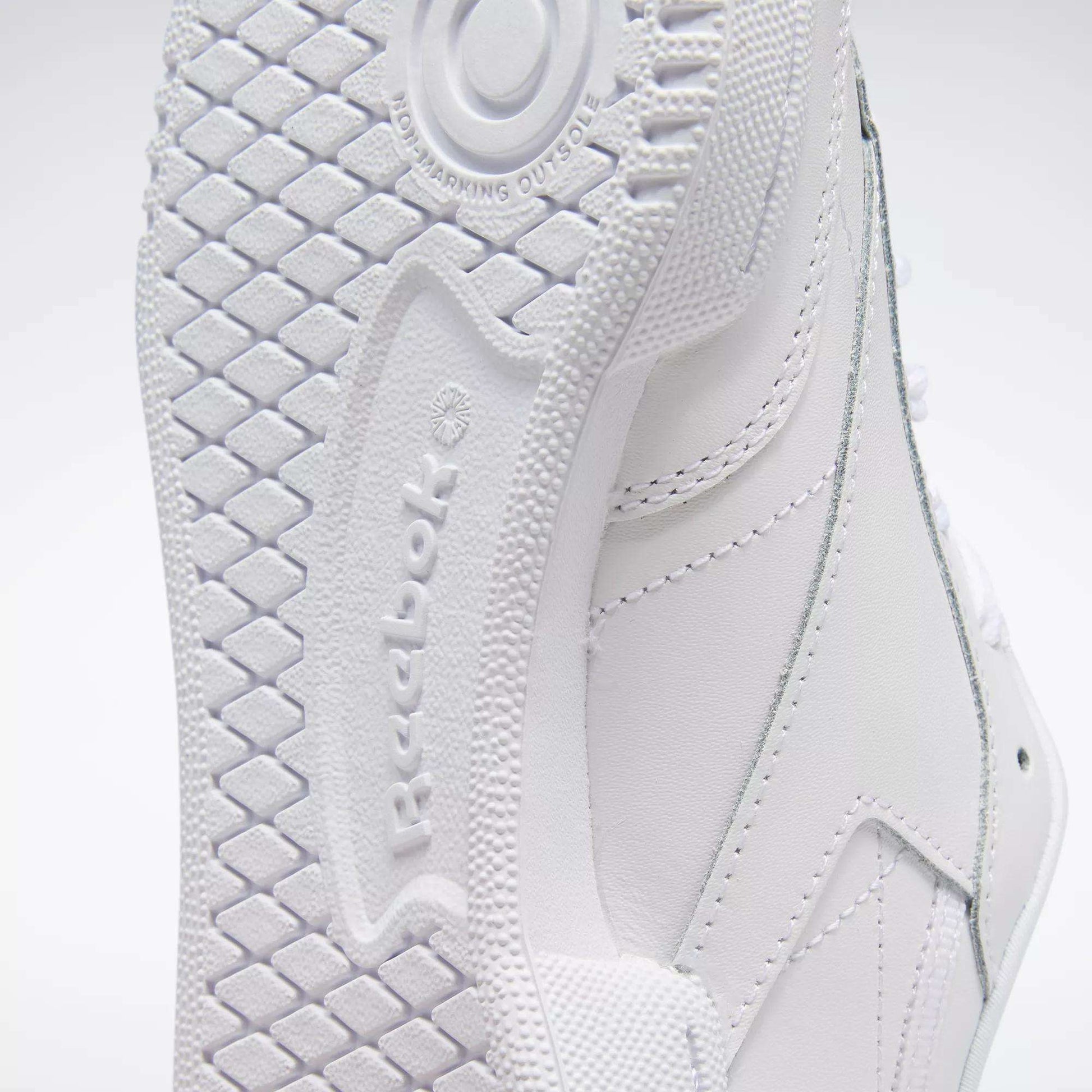 Close-up of the sole and side of Reebok Kids' Club C Shoes - Grade School, highlighting the detailed tread, textured logo, stitching on soft leather uppers, and a high-abrasion rubber outsole with diamond pattern and circular heel design.