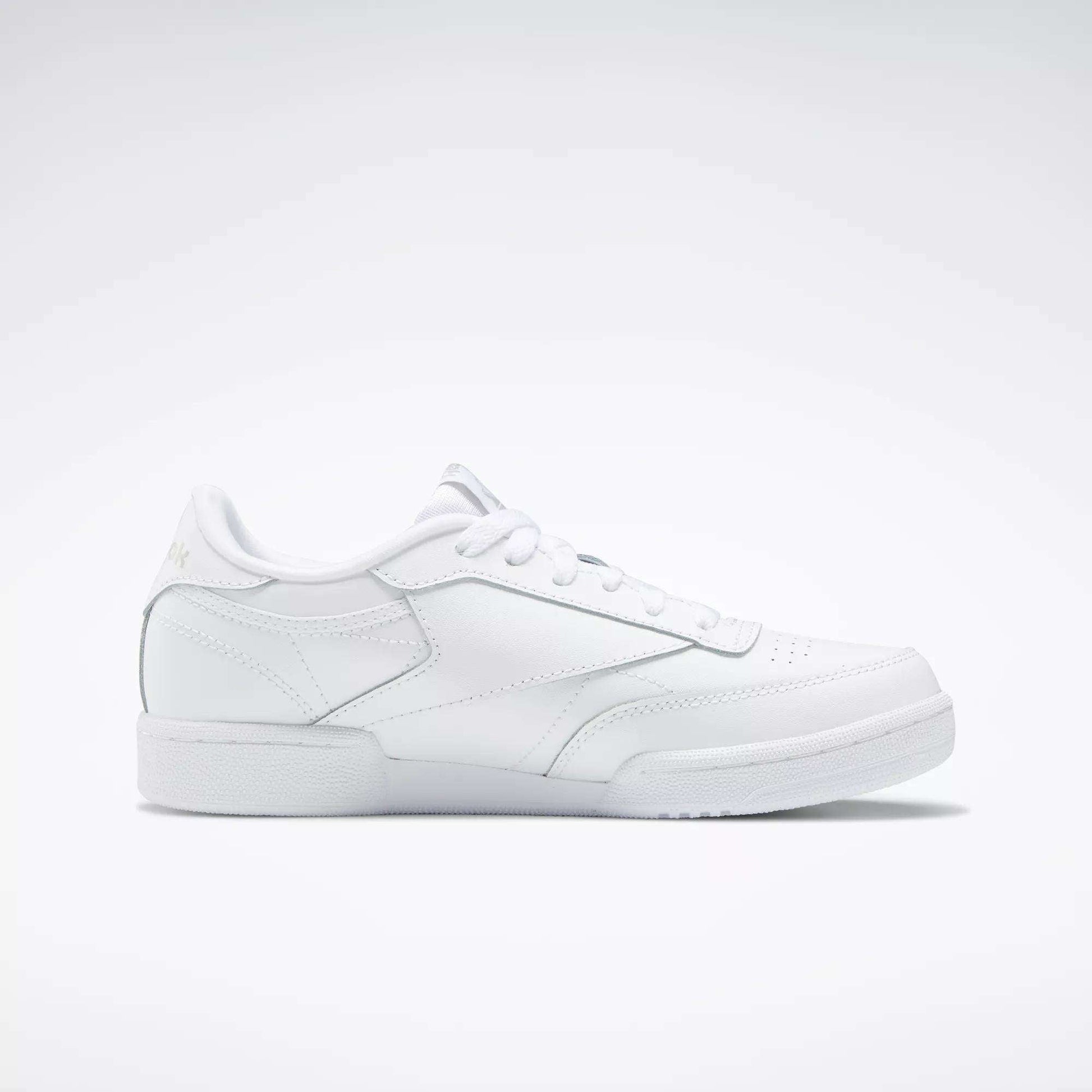 The Reebok Kids' Club C Shoes - Grade School feature soft white leather uppers with minimal branding, shown in a side profile against a light gray background—an effortlessly simple, classic court shoe design.