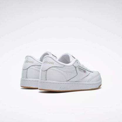 The Reebok Kids' Club C Shoes – Grade School feature soft white leather uppers, subtle grey branding, and a gum sole. Shown on a light background, the sneakers are angled to highlight the back and side views.