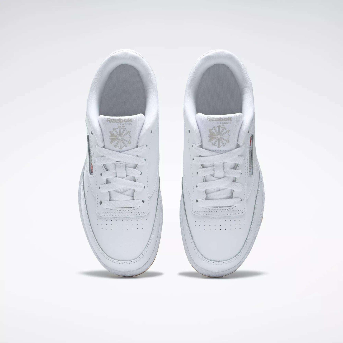 A pair of Kids' Club C Shoes - Grade School by Reebok, seen from above, with clean white leather uppers, laces, perforated toes, and Reebok logos on the tongues. The classic court style is displayed side by side on a light background.