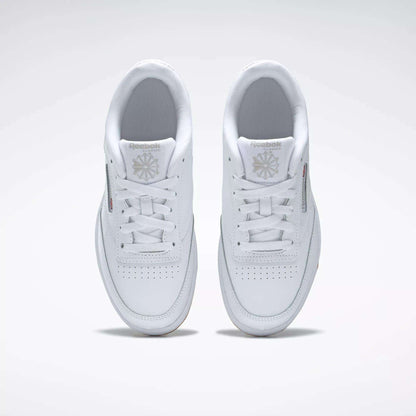 A pair of Kids' Club C Shoes - Grade School by Reebok, seen from above, with clean white leather uppers, laces, perforated toes, and Reebok logos on the tongues. The classic court style is displayed side by side on a light background.
