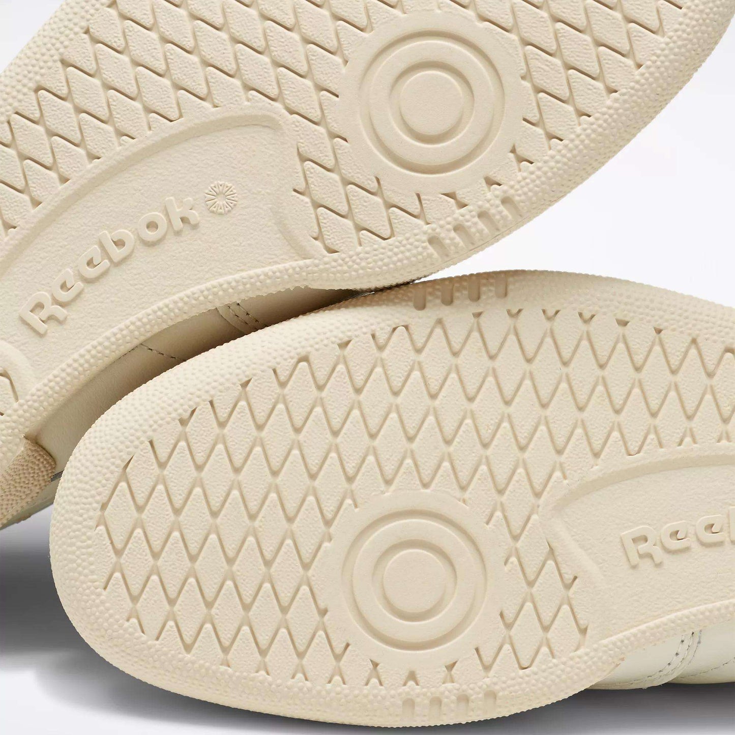Close-up of the beige rubber soles of Reebok Club C 85 Vintage Shoes, showing a diamond-patterned tread, circular grip details, and the embossed Reebok logo.