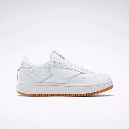 The Reebok Women's Club C Double Shoes are white, low-top sneakers with white laces, subtle stitching, and a light brown rubber sole with a platform midsole, shown in profile against a plain white background.