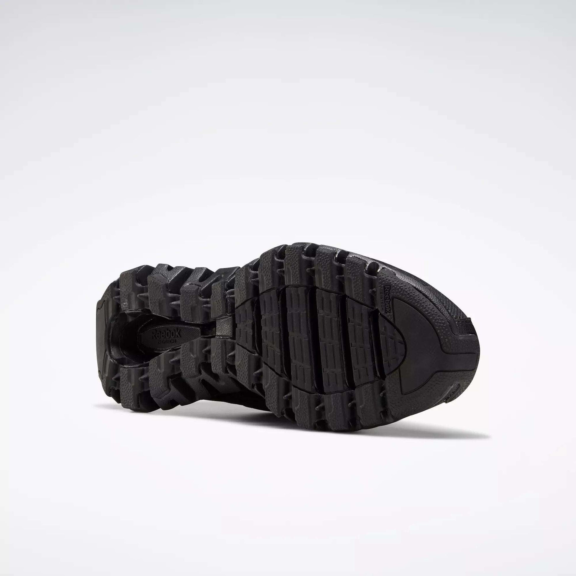 Close-up of the black, rugged sole on Reebok Men's ZigWild Trail 6 Shoes, showcasing deep treads and grooves in a trail-inspired design against a plain light background.