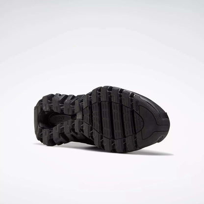 Close-up of the black, rugged sole on Reebok Men's ZigWild Trail 6 Shoes, showcasing deep treads and grooves in a trail-inspired design against a plain light background.