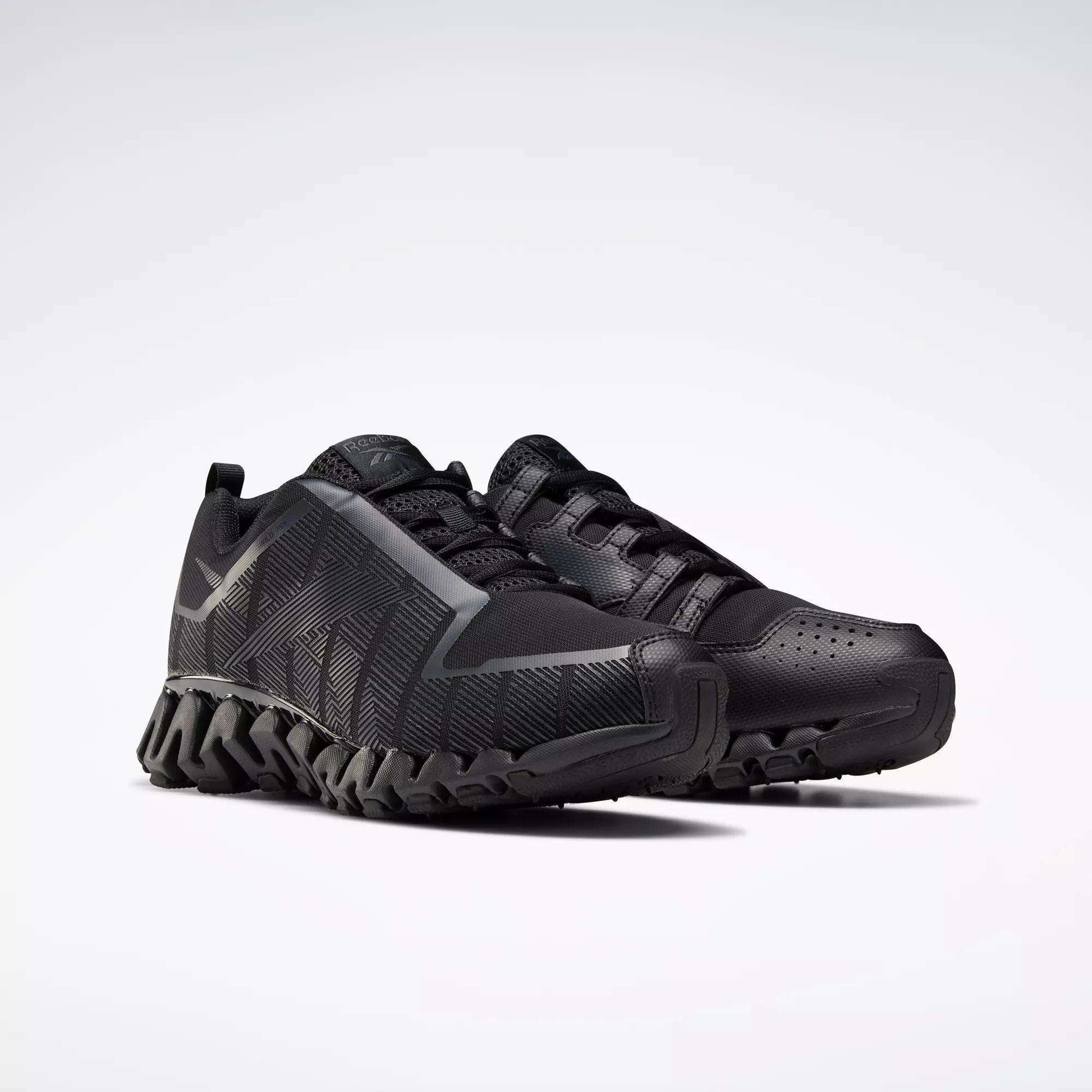 A pair of Reebok Men's ZigWild Trail 6 Shoes in black, with textured soles, geometric side patterns, and enhanced cushioning, displayed on a plain light background.