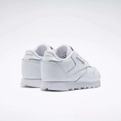 A pair of Reebok Kids' Classic Leather Shoes - Baby & Toddler in white, shown from the back and side angles against a plain white background.
