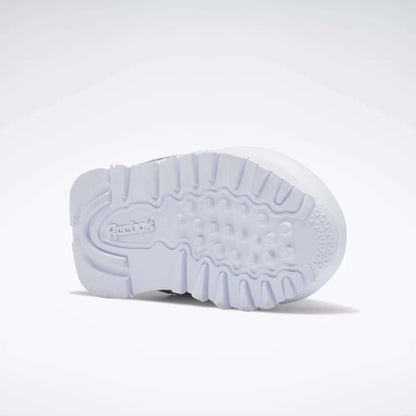 The image shows the white rubber sole of Reebok Kids' Classic Leather Shoes for babies and toddlers, viewed from below. The textured pattern provides grip, and the Reebok logo appears in raised letters near the heel.