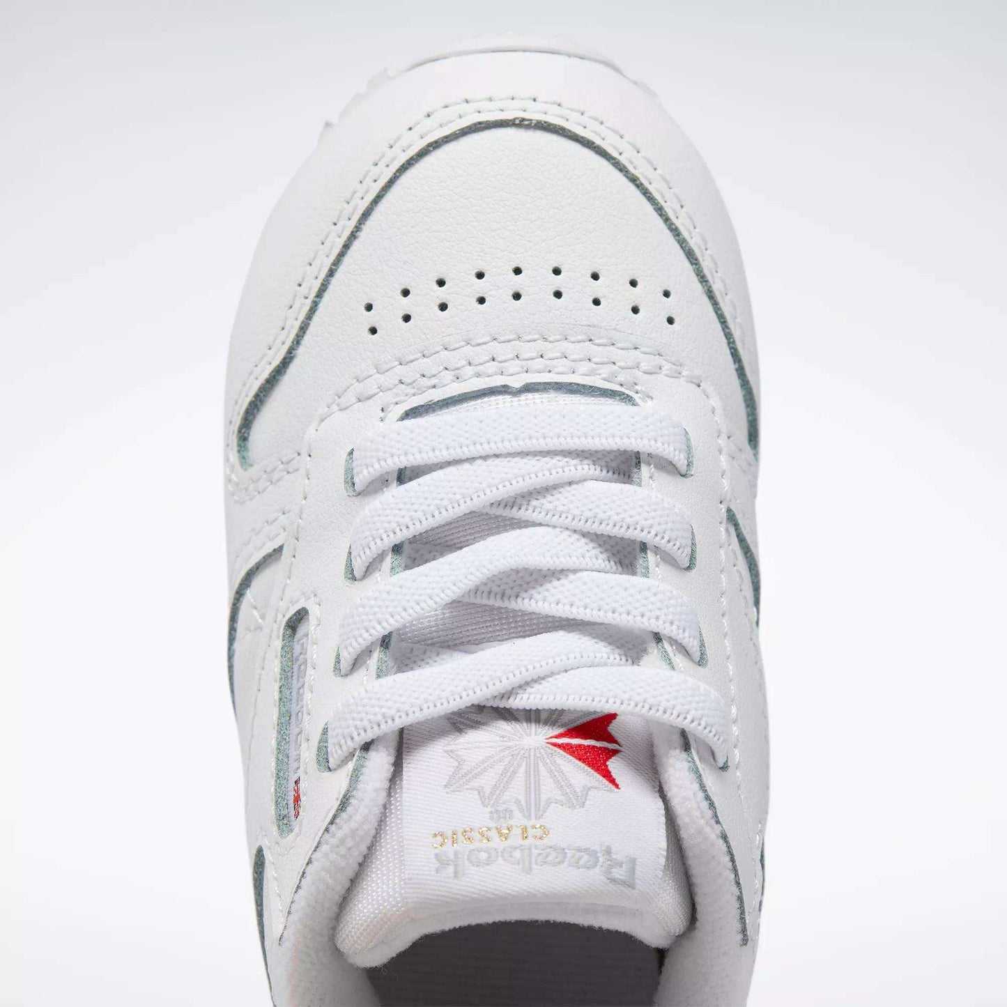 Close-up of Kids' Classic Leather Shoes - Baby & Toddler by Reebok, featuring white leather, laces, perforated toe box, and tongue with silver and red Reebok branding—ideal for active toddlers.