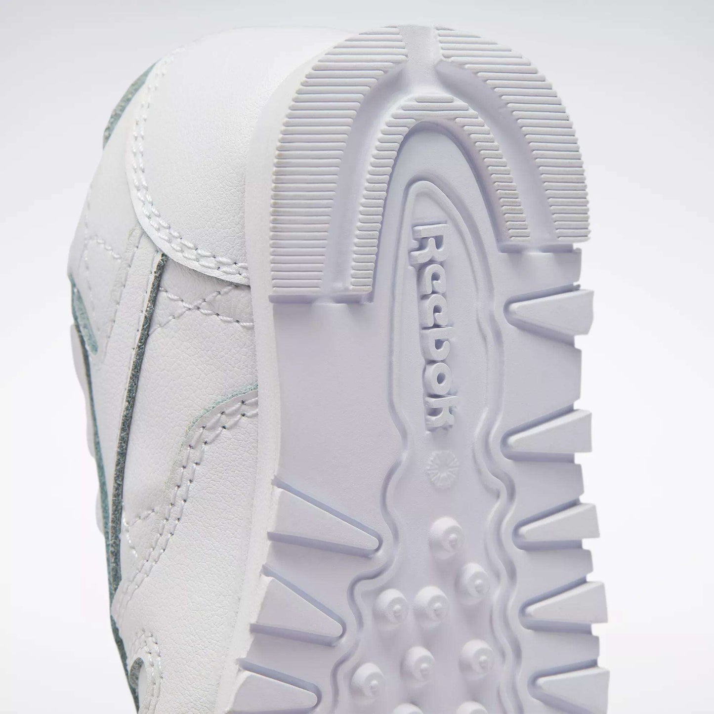 Close-up of the sole on Reebok Kids' Classic Leather Shoes for babies and toddlers, showing textured grip patterns, embossed Reebok logo, leather material, and visible stitching.