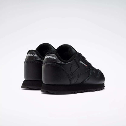 A pair of Kids' Classic Leather Shoes - Baby & Toddler by Reebok in black, shown from the back and side with visible Reebok logos on the heel and outer side, classic old-school style on a plain white background.