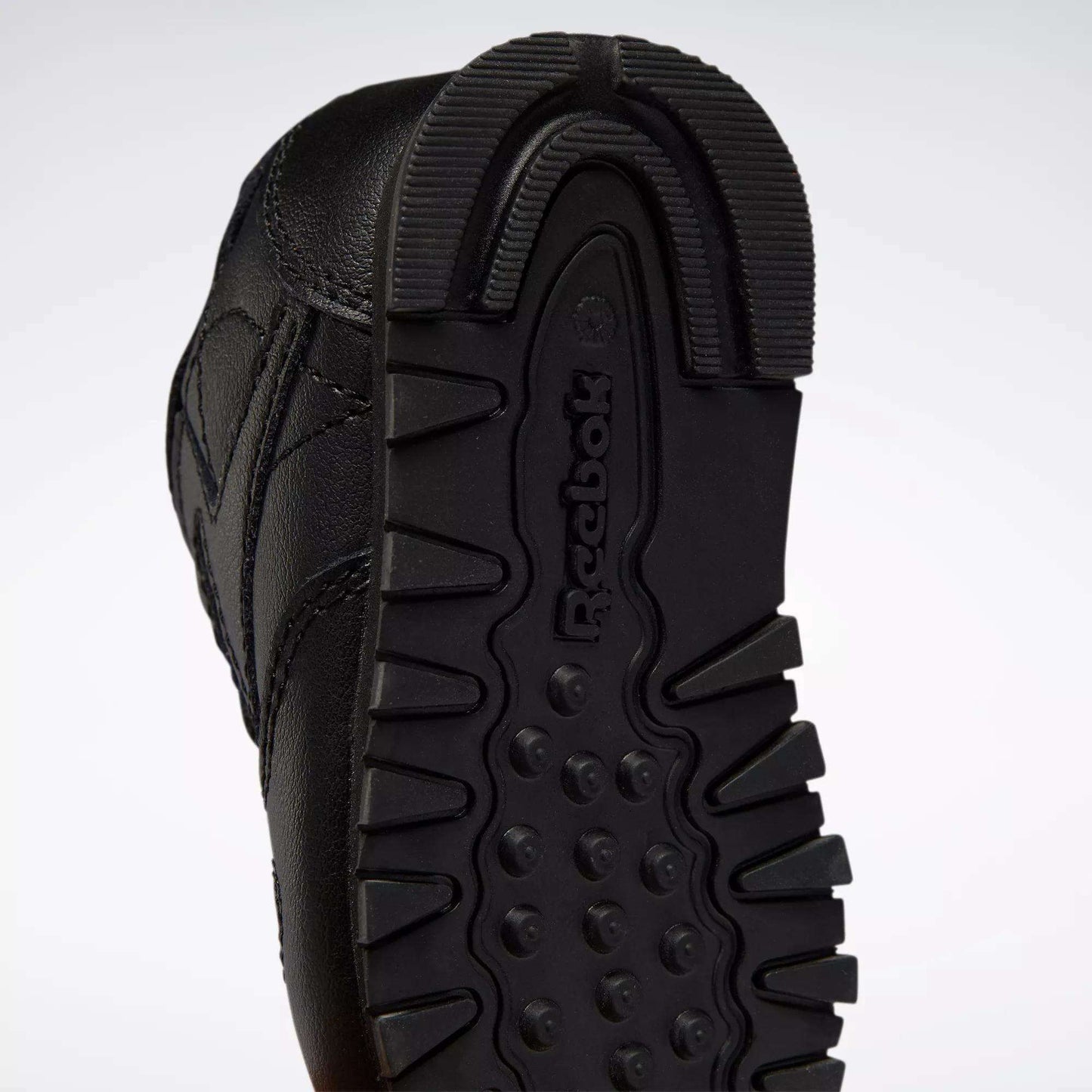 Close-up of the black rubber sole on Reebok Kids' Classic Leather Shoes for babies and toddlers, featuring a textured tread pattern and the embossed Reebok logo—an iconic detail on classic sneakers.