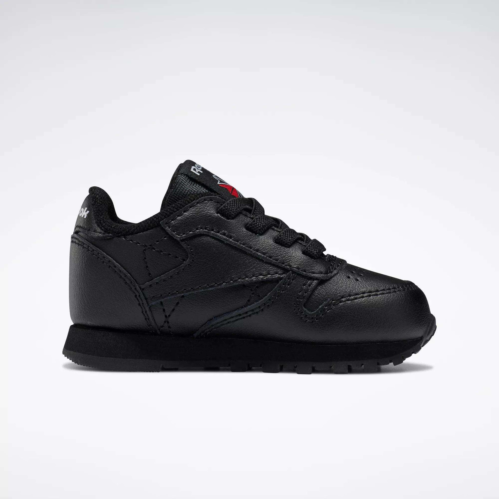 The Reebok Kids' Classic Leather Shoes - Baby & Toddler feature a black leather design with black laces and sole, shown in side profile on a white background for a timeless old-school sneaker look.