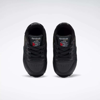 A pair of Reebok Kids' Classic Leather Shoes for baby & toddler in black, viewed from above with the Reebok logo and a red and white emblem on the tongues, set against a plain white background—ideal for young fans of classic sneakers.