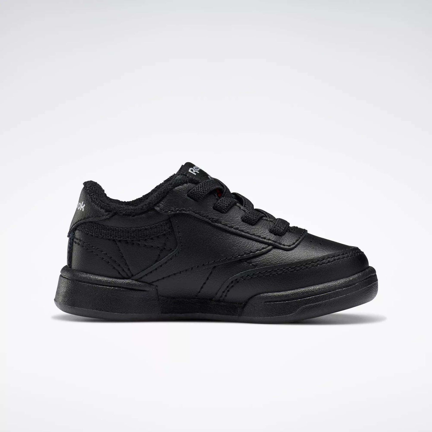 A single black Reebok Kids' Club C Shoe for babies and toddlers, featuring soft leather, black laces, and stitching details, is displayed in side profile against a plain white background.