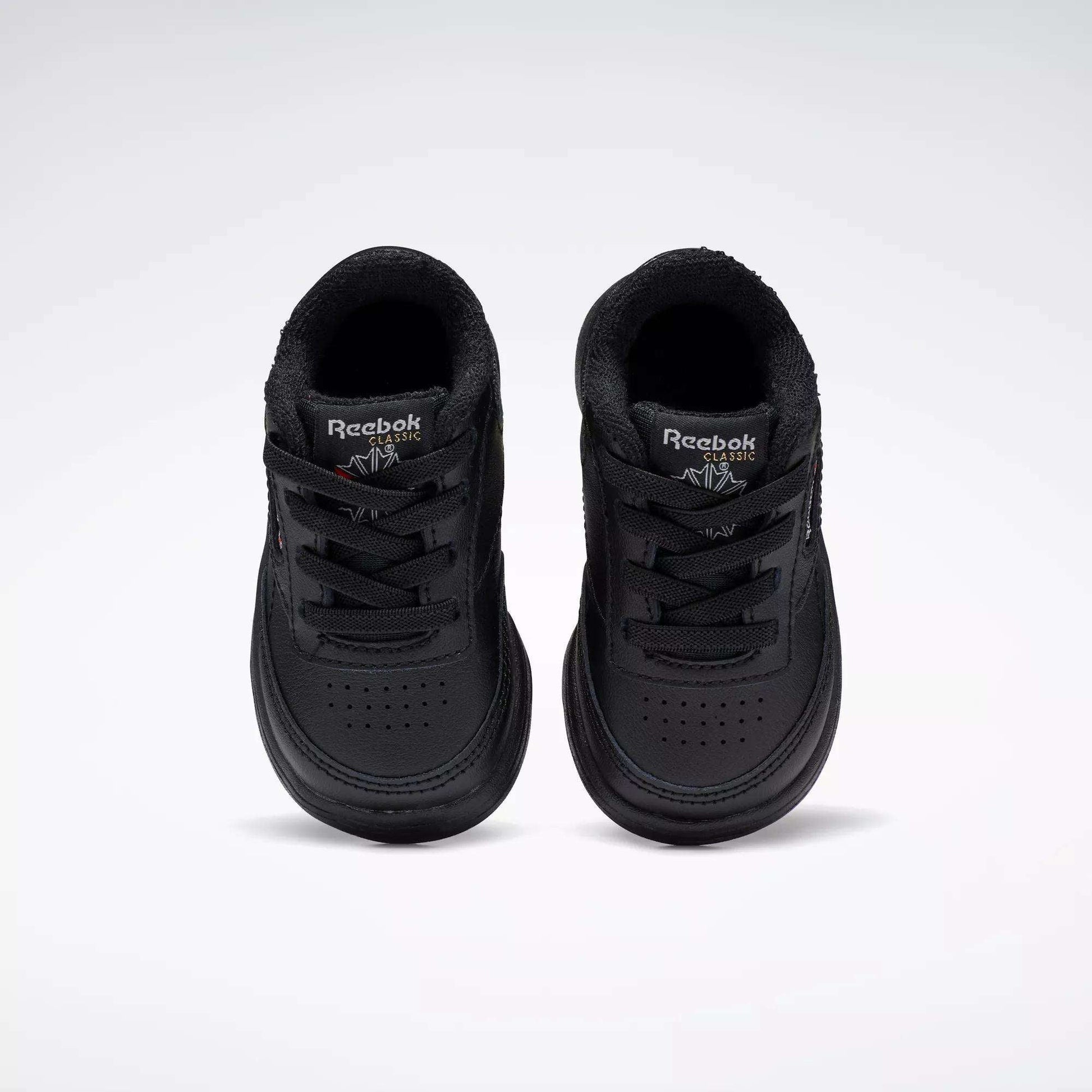 A pair of Reebok Kids' Club C Shoes for babies and toddlers, in black soft leather, are displayed side by side on a plain white background, viewed from above.