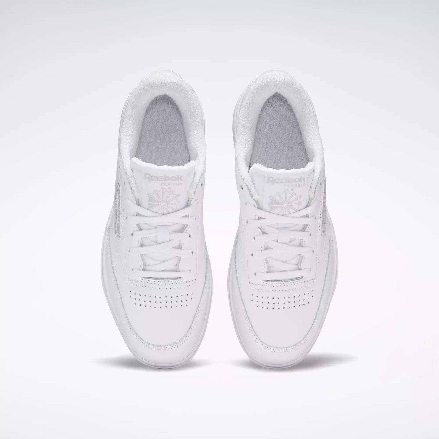 A pair of Reebok Women's Club C Double Shoes in white, seen from above on a light background, highlighting the perforated toe and Reebok logo on each tongue.