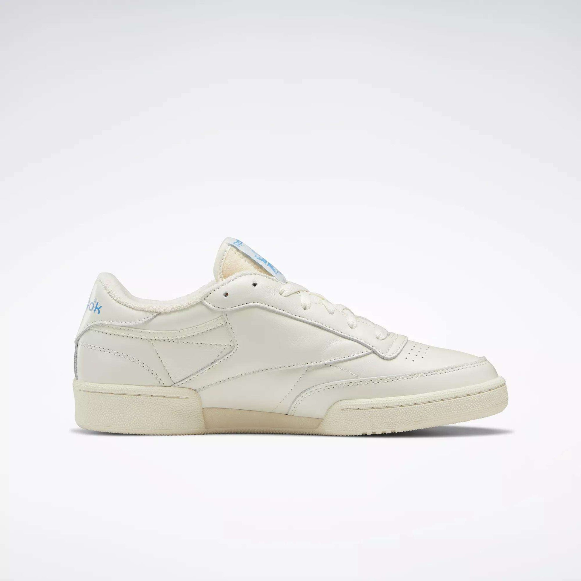 The Reebok Club C 85 Vintage Shoes are shown in side profile on a white background, featuring a cream leather upper, lightweight cushioning, and subtle blue branding on the heel and tongue.